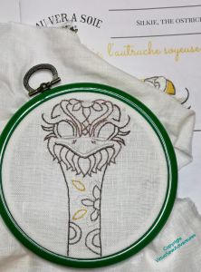 Green Flexihoop showing Silkie the Ostrich with outlines in place and some of the white padded satin stitch around his beak complete.