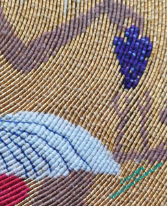 Close up of a section of the embroidered piece, showing gold threads couched with silk, showing a had holding a bunch of grapes, and part of a pleated kilt.