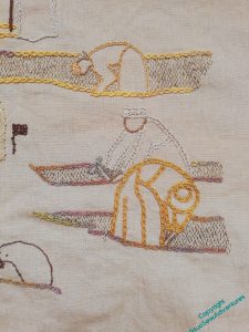 A portion of the embroidered depiction of an excavation in browns and golds, using different intricate line stitches to help differentiate the different figures. Tiny running stitches run vertically in some sections to suggest the vertical wall of a trench.