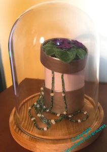 Parlour dome containing a second effort to display the clump of violets and the necklace. Raising the height of the box is an improvement, but it is still too wide.