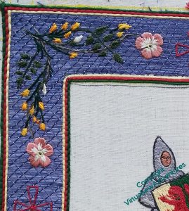 Close up of the top left corner of the border. The background is trellis couching in several shades of blue, the edges are yellow, red and green, and the corner motif shows sprigs of broom intertwined with dog roses. The rose stem used a fawn and a brown thread twisted together.