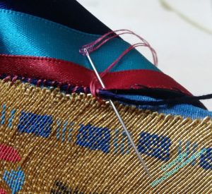 The ribbon is being attached to the gold using red silk over a navy thread.