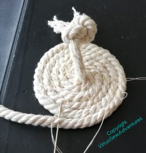 The beginning of the coiled pot in piping cord. A knot keeps the end from unravelling, and stands up straight out of the flat base which is all that has been done so far.