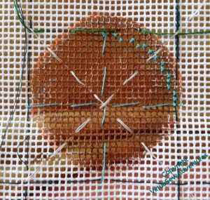 A small section of canvas. Part of it has been painted brown, and there are tacking stitches to divide up the square and plan a circular outline.