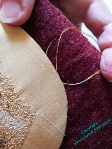 Close up of the use of a curved needle to ladder stitch the golden silk to the burgundy chenille.