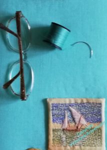 Against a turquoise linen background, there's a pair of spectacles, a reel of turquoise thread, and a curved needle.
In the lower right hand corner is the little Felucca picture, which is presumably about to be stitched down.