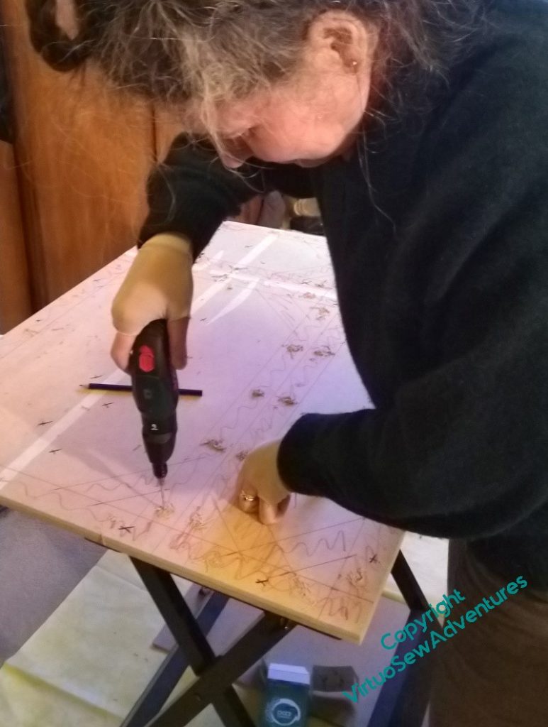 The board is now on a workbench and you can see Rachel, a white woman with greying hair, drilling holes in it.