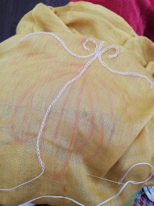 The fabric is open over a lap, and you can see rough chalk lines and a few rows of chain stitch.