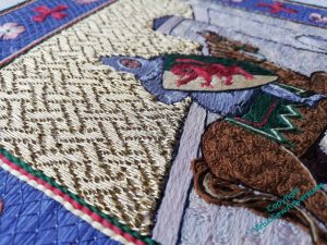 Oblique view across the gold basketweave couching towards William and the castle