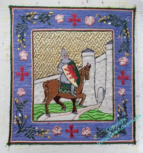 William Marshall on his bay horse, visiting the Chateau de Tancarville to show off. The background is basketweave pattern underside couching, and the picture is surrounded by a blue border with red Templar crosses at the cardinal points, and sprigs of broom and dog roses in the corners.