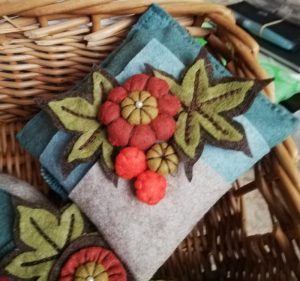 A small square felt cushion, presented on the diagonal and decorated with felt leaves, flower and buds. The shoes will be hung from this to create a mobile.