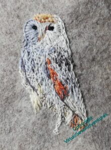 The owl is taking shape in a tangle of white, grey, and cream stitching.